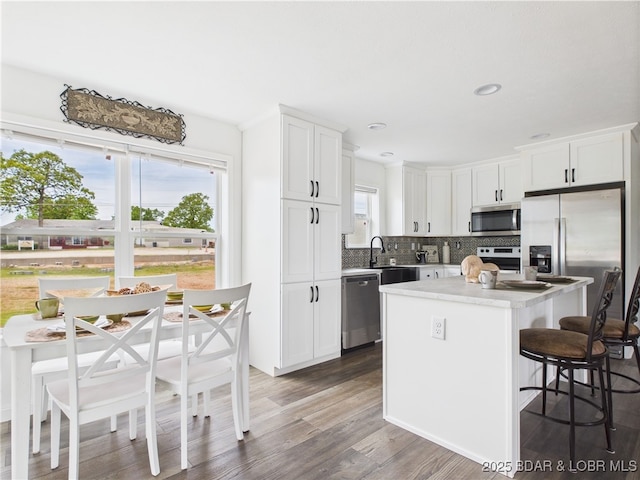 kitchen featuring stainless steel appliances, tasteful backsplash, wood finished floors, a kitchen bar, and a kitchen island