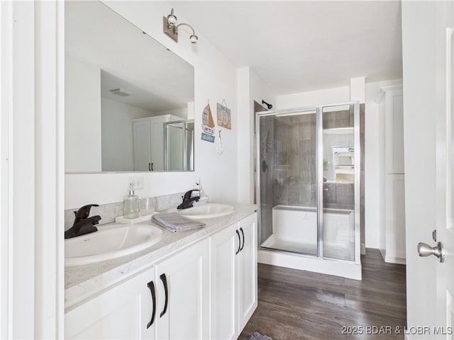 full bath with a sink, double vanity, a shower stall, and wood finished floors