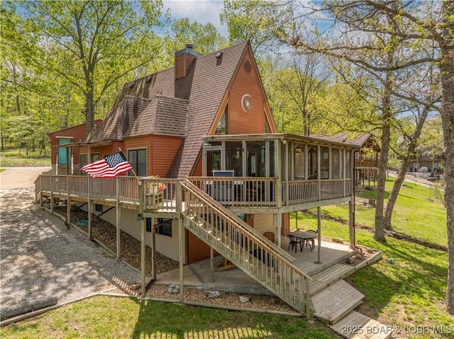 back of house featuring roof with shingles, a wooden deck, a sunroom, and stairway