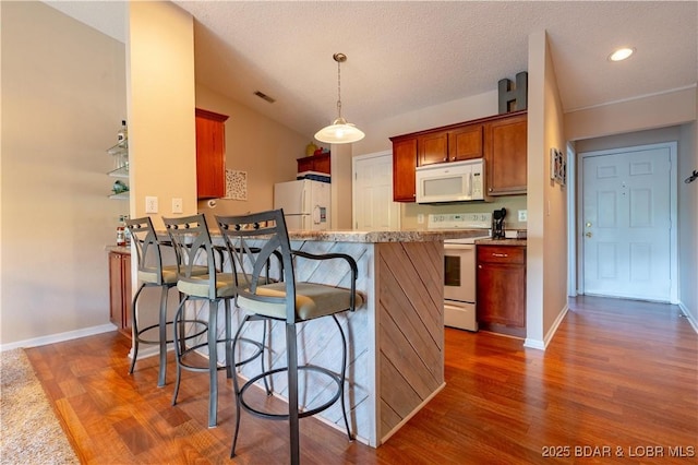 58 Jonathan Dr Unit 4B, Lake Ozark, MO 65049 - kitchen featuring white appliances, dark wood-style flooring, a peninsula, a breakfast bar area, and baseboards