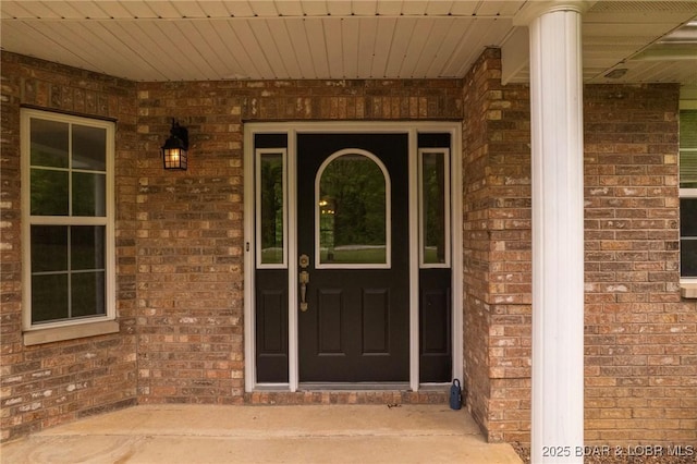 doorway to property featuring covered porch and brick siding