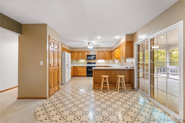 kitchen featuring black appliances, a peninsula, light countertops, baseboards, and a ceiling fan