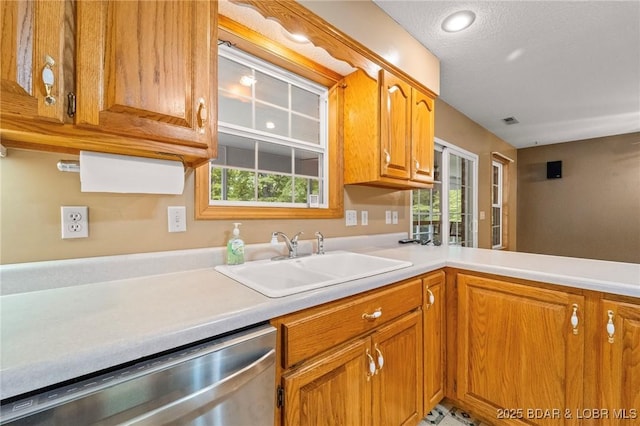 kitchen featuring stainless steel dishwasher, a sink, brown cabinetry, light countertops, and healthy amount of natural light