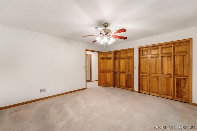 unfurnished bedroom with light colored carpet, baseboards, multiple closets, and ceiling fan