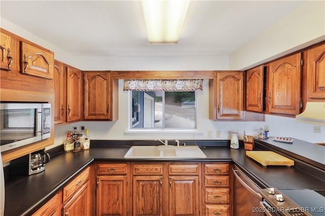 kitchen featuring appliances with stainless steel finishes, a sink, brown cabinetry, and dark countertops