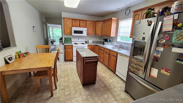 kitchen with white appliances, light countertops, a center island, a sink, and brown cabinetry