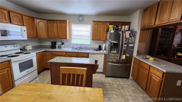kitchen with white appliances, brown cabinetry, a center island, and light floors