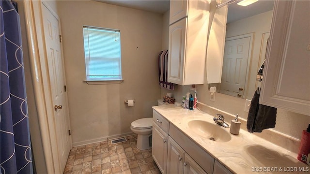 bathroom featuring toilet, vanity, baseboards, and stone finish floors