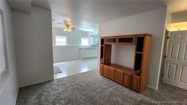 unfurnished living room with ceiling fan, carpet floors, a sink, and baseboards
