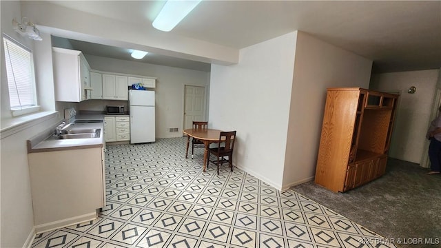 kitchen featuring freestanding refrigerator, white cabinets, a sink, and baseboards