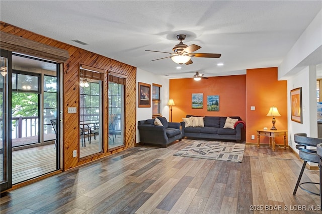 living area with ceiling fan, wood-type flooring, and wooden walls