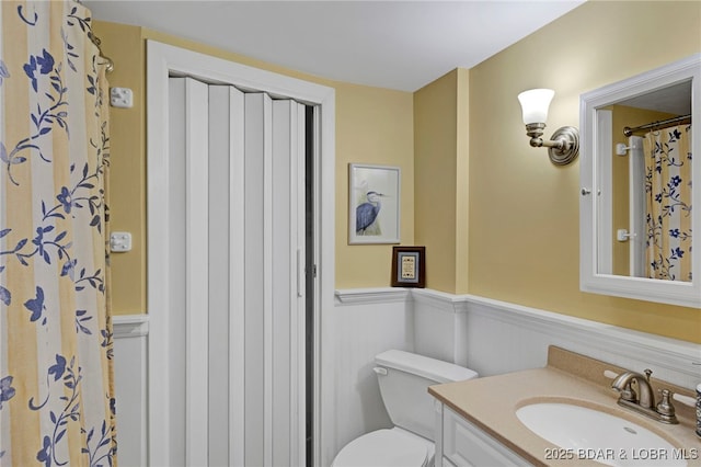 full bathroom featuring wainscoting, vanity, and toilet
