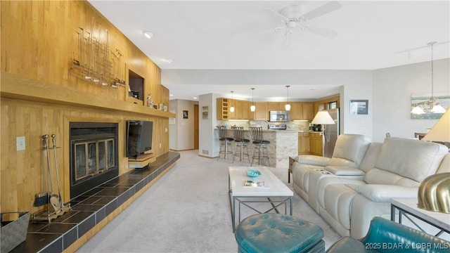 living room featuring ceiling fan, a tiled fireplace, light carpet, track lighting, and wooden walls