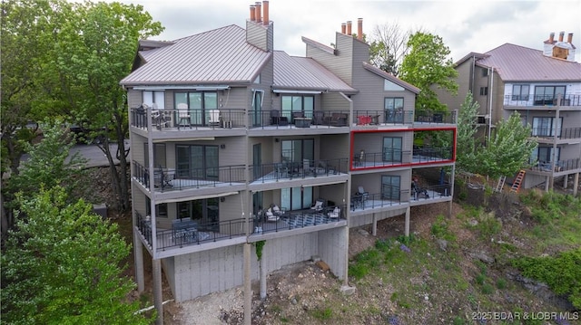 rear view of house featuring a chimney, metal roof, and a balcony