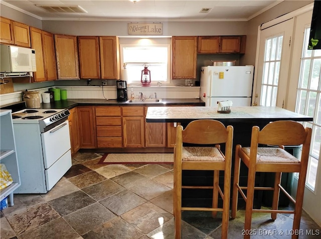 kitchen featuring white appliances, ornamental molding, plenty of natural light, brown cabinets, and stone tile flooring
