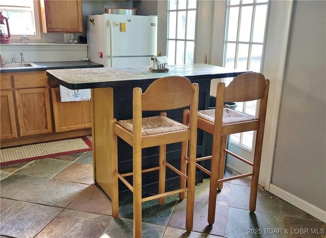kitchen featuring freestanding refrigerator, a sink, brown cabinets, and stone finish floors
