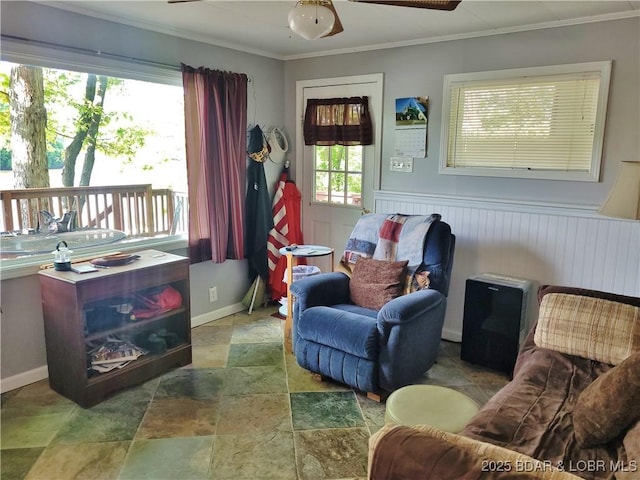 sitting room featuring stone finish floors, ornamental molding, ceiling fan, and wainscoting