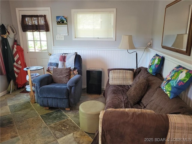 living area featuring stone tile flooring and wainscoting