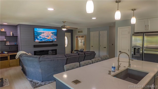 living room with ceiling fan, a glass covered fireplace, light wood-style floors, and recessed lighting