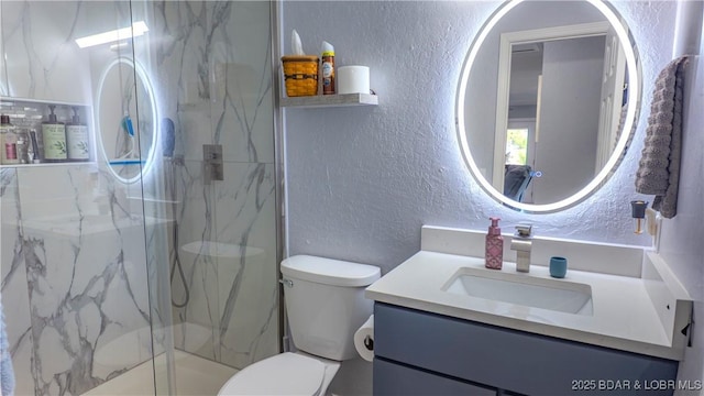 bathroom featuring a textured wall, a marble finish shower, vanity, and toilet