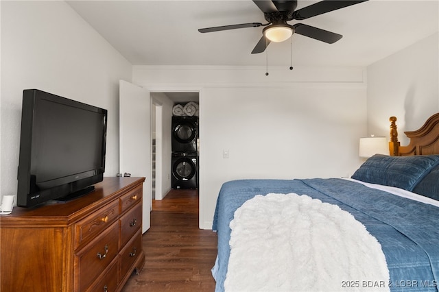 bedroom featuring stacked washer / dryer, dark wood-style floors, and a ceiling fan