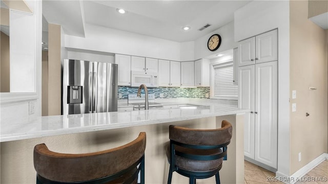 kitchen featuring white appliances, a kitchen breakfast bar, white cabinetry, light stone counters, and decorative backsplash