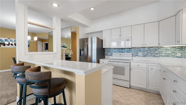 kitchen with white appliances, a kitchen bar, white cabinets, backsplash, and recessed lighting