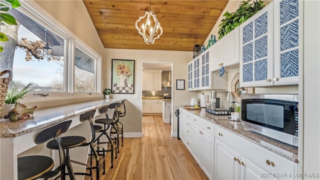 kitchen with stainless steel microwave, white cabinetry, light wood finished floors, wood ceiling, and glass insert cabinets
