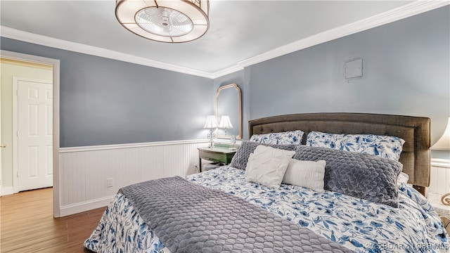 bedroom featuring wood finished floors, wainscoting, crown molding, and baseboards