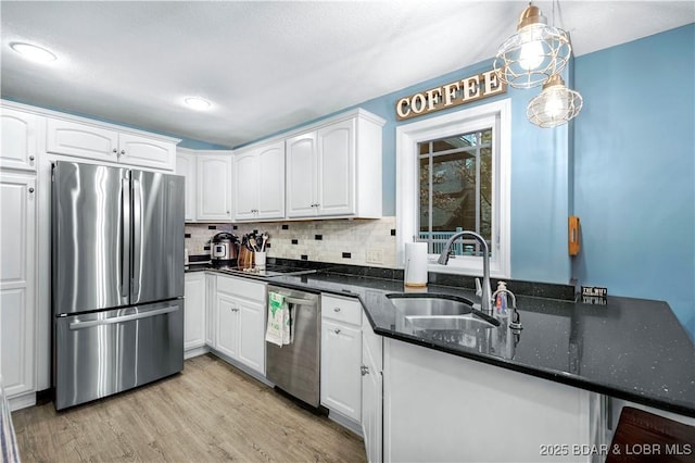 kitchen with appliances with stainless steel finishes, a sink, white cabinetry, dark stone countertops, and tasteful backsplash
