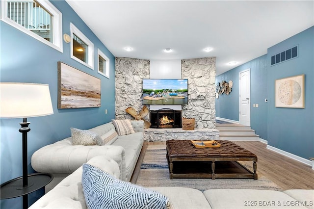 living room featuring wood finished floors, a stone fireplace, baseboards, and recessed lighting