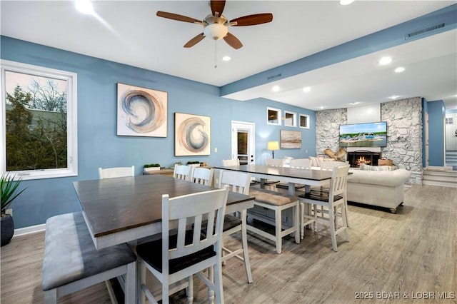 dining space with light wood finished floors, ceiling fan, a stone fireplace, recessed lighting, and baseboards