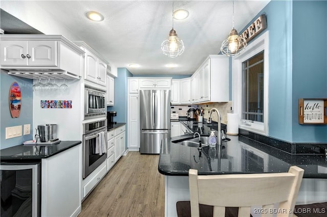 kitchen with appliances with stainless steel finishes, a peninsula, beverage cooler, light wood finished floors, and white cabinets