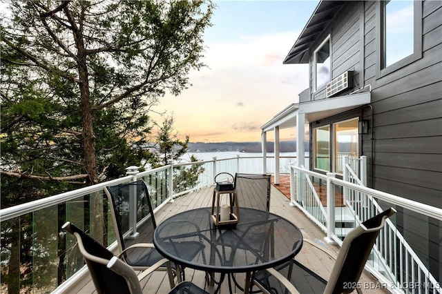 balcony at dusk featuring outdoor dining area and a deck with water view