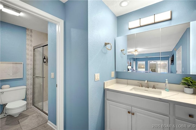 full bath with toilet, a stall shower, vanity, and a textured wall