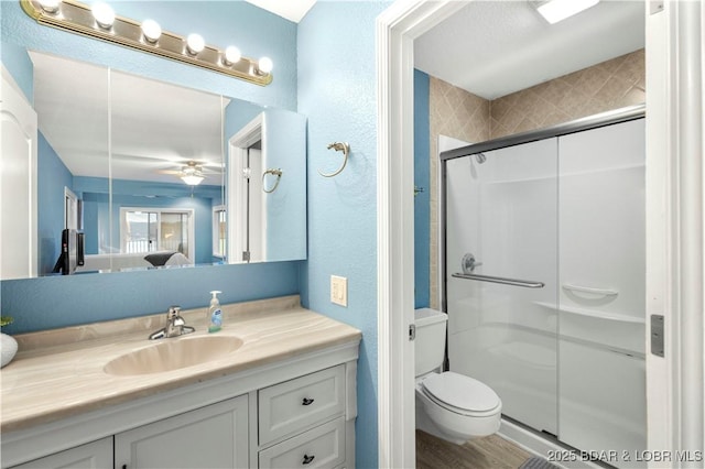 ensuite bathroom featuring a shower stall, vanity, toilet, wood finished floors, and a ceiling fan