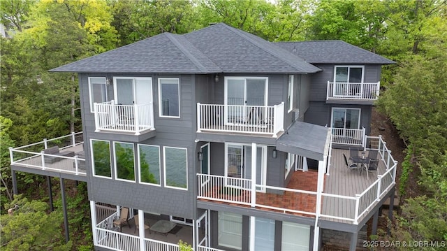 rear view of property with roof with shingles, a balcony, and a forest view
