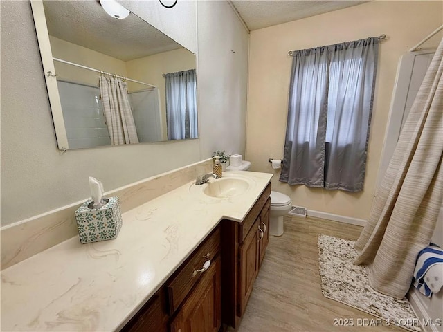 full bath with wood finished floors, baseboards, toilet, vanity, and a textured ceiling
