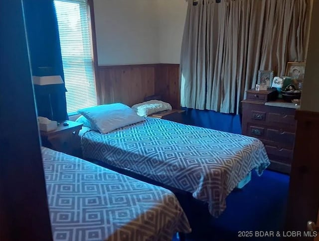 bedroom featuring multiple windows, wainscoting, and wood walls