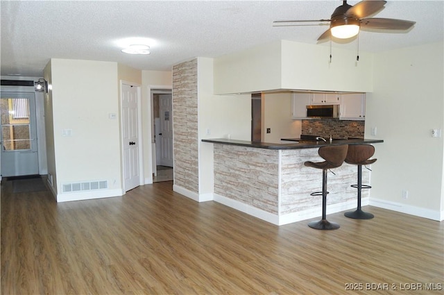 kitchen with stainless steel microwave, a textured ceiling, wood finished floors, baseboards, and dark countertops