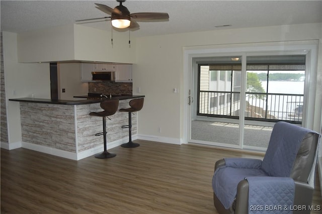 living room featuring baseboards, a ceiling fan, wood finished floors, and a textured ceiling