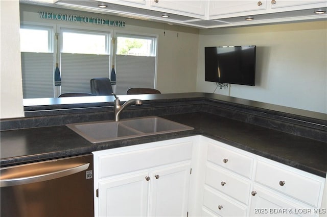 kitchen featuring stainless steel dishwasher, a sink, dark countertops, and white cabinets
