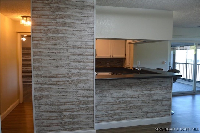 kitchen featuring dark countertops, a textured ceiling, wood finished floors, baseboards, and a sink
