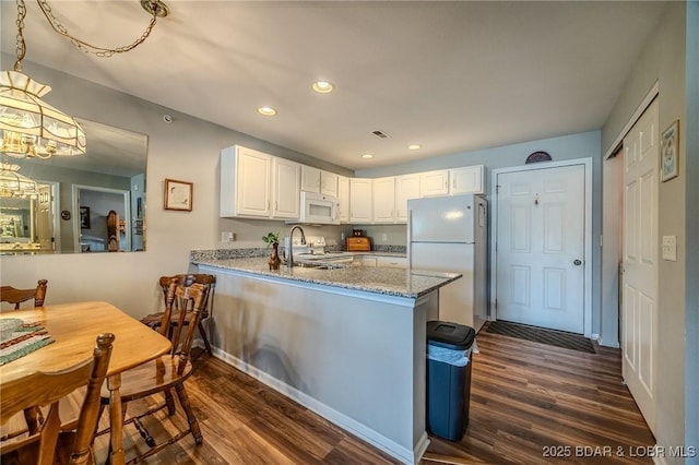 kitchen with white appliances, dark wood-type flooring, light stone counters, recessed lighting, and a peninsula