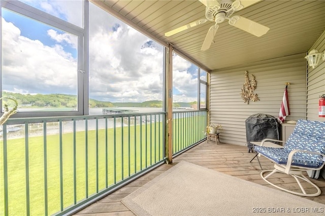 sunroom with ceiling fan and a water view