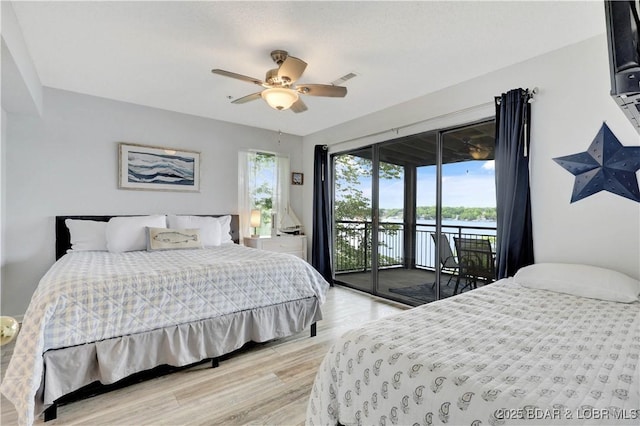 bedroom with access to exterior, light wood-type flooring, a ceiling fan, and a water view