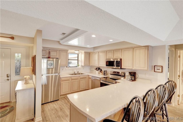 kitchen featuring stainless steel appliances, light brown cabinets, light wood-style floors, a sink, and a peninsula