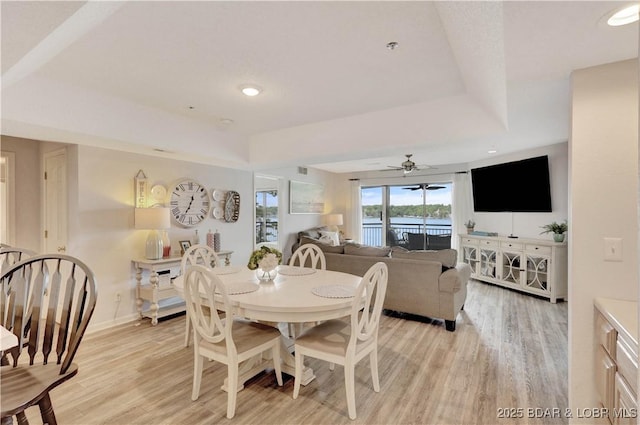 dining area featuring light wood-style flooring, a raised ceiling, a ceiling fan, and baseboards