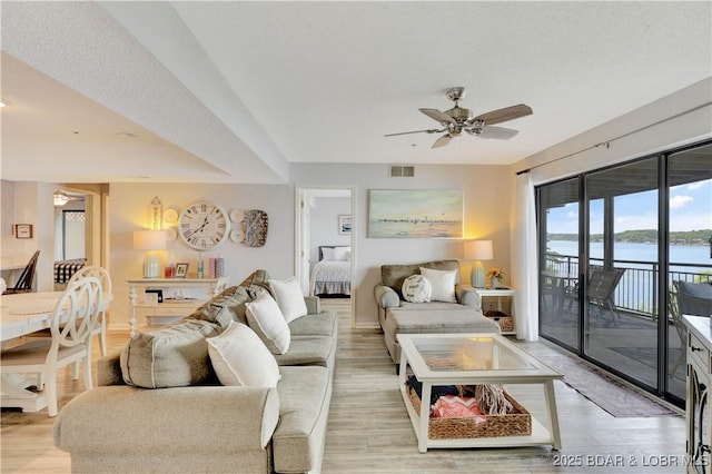 living area featuring a ceiling fan, light wood finished floors, a water view, and baseboards