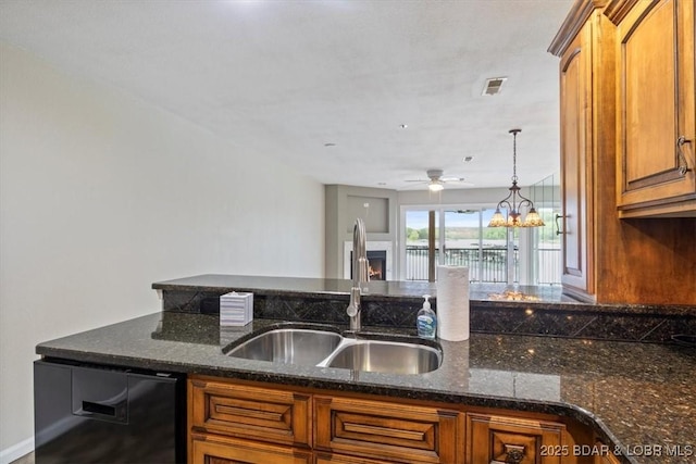 kitchen with a sink, brown cabinetry, black dishwasher, ceiling fan, and dark stone countertops